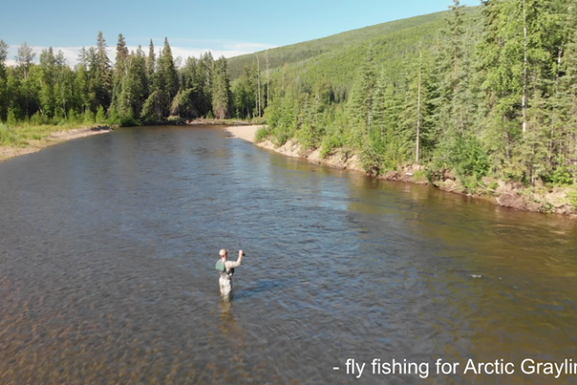 a man standing next to a body of water surrounded by trees
