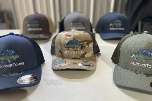 Five Ak River Tours hats on display, in various colors, with a fish logo.