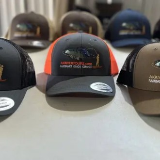 Four baseball caps with fish logos displayed on a table.
