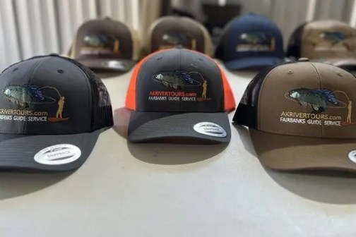 Four baseball caps with fish logos displayed on a table.